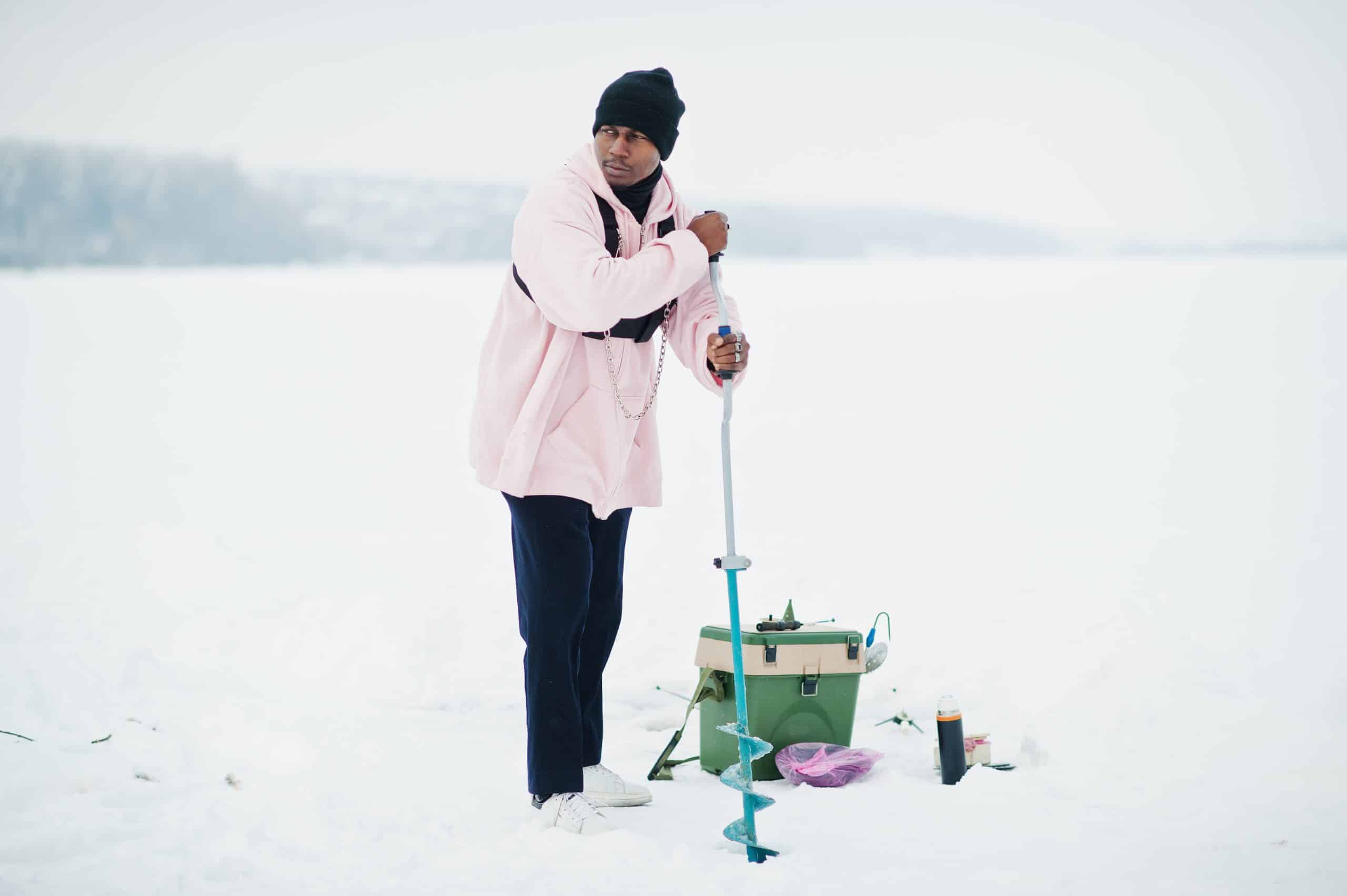 Angler drilling a hole in thick lake ice with a hand auger before ice fishing