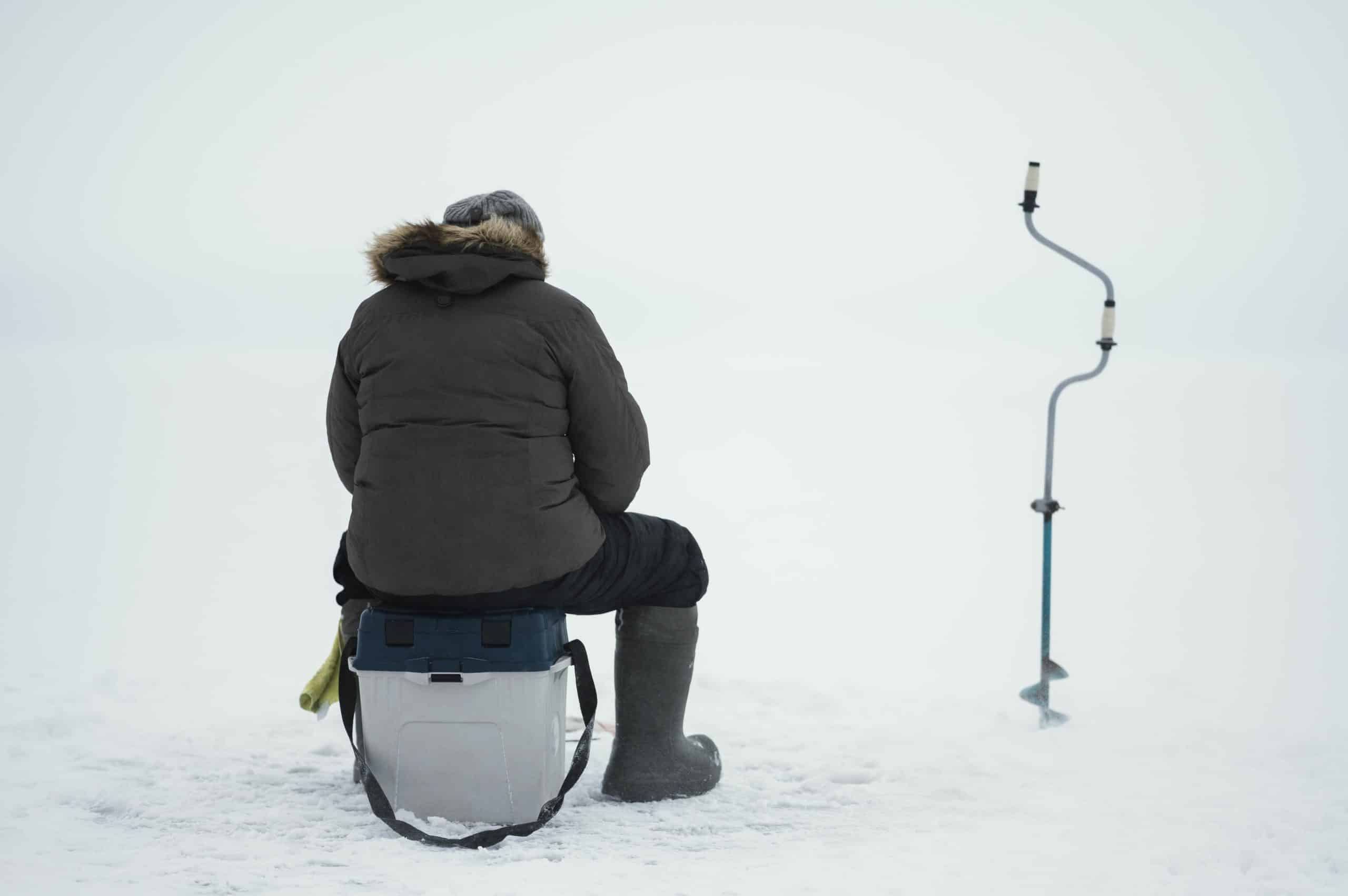 Angler with ice fishing gear including rod, sled and shelter on a frozen lake